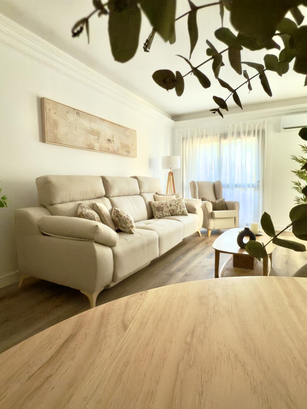Salón luminoso con sofá claro, butaca orejera y mesa de centro de madera